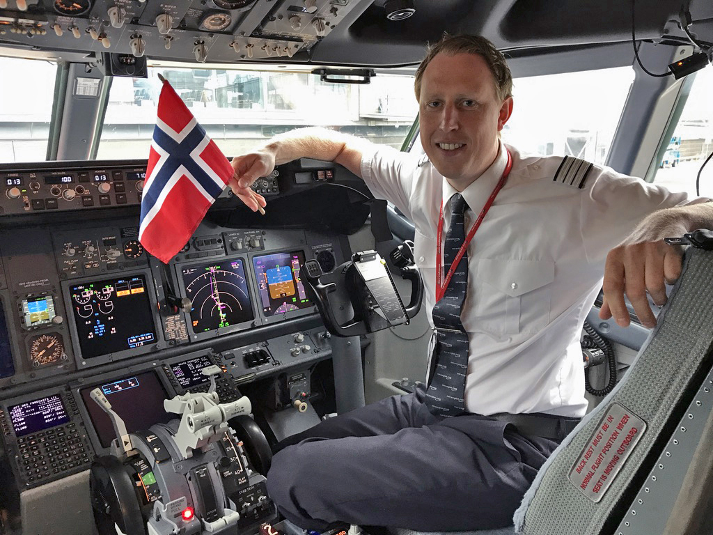 Pilot Mats Rove sitting in the cockpit holding a Norwegian flag